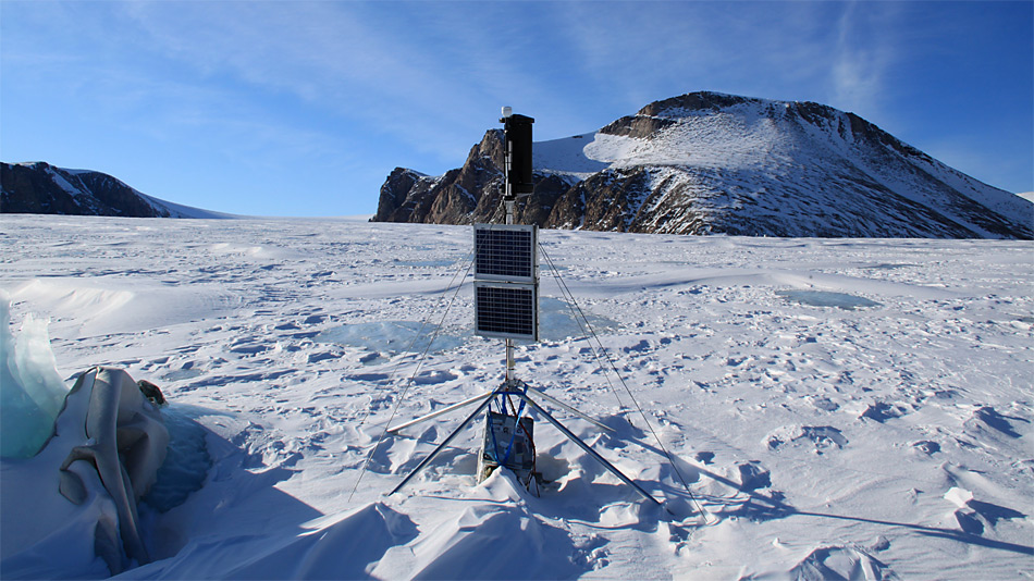 Passive Seismik/ GPS Station am A.P. Olsen Ice Cap. Zu sehen sind (von oben beginnend) GPS Antenne, Windrad, Solar Panels und die Alukiste, in der sich Messgeräte befinden. Foto: ZAMG/Daniel Binder