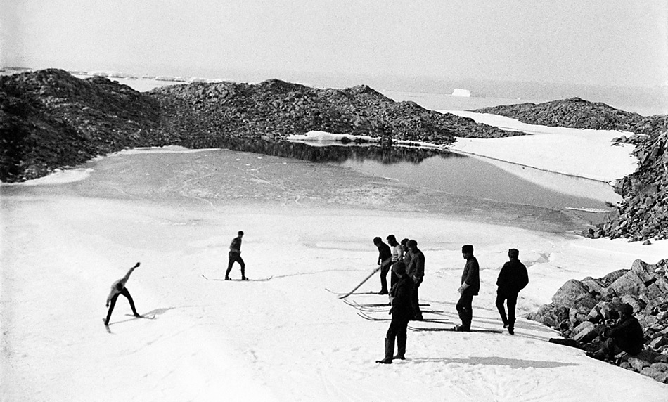 Australische Skifahrer auf dem antarktischen Kontinent. Landeinwärts südöstlich der Basisstation bei Cape Denison. Im Hintergrund ein während des antarktischen Sommers aufgetauter Gletschersee (Xavier Mertz, wahrscheinlich Mitte Februar 1912; Continental Size; Mitchell Library, State Library of New South Wales).